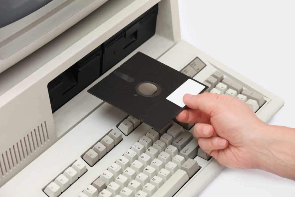Invoegen van oude diskette in een vintage oude computer uit de jaren tachtig, met geïntegreerde schijfstationmonitor en toetsenbord. Retro revivalstijl met afgeronde hoeken.
